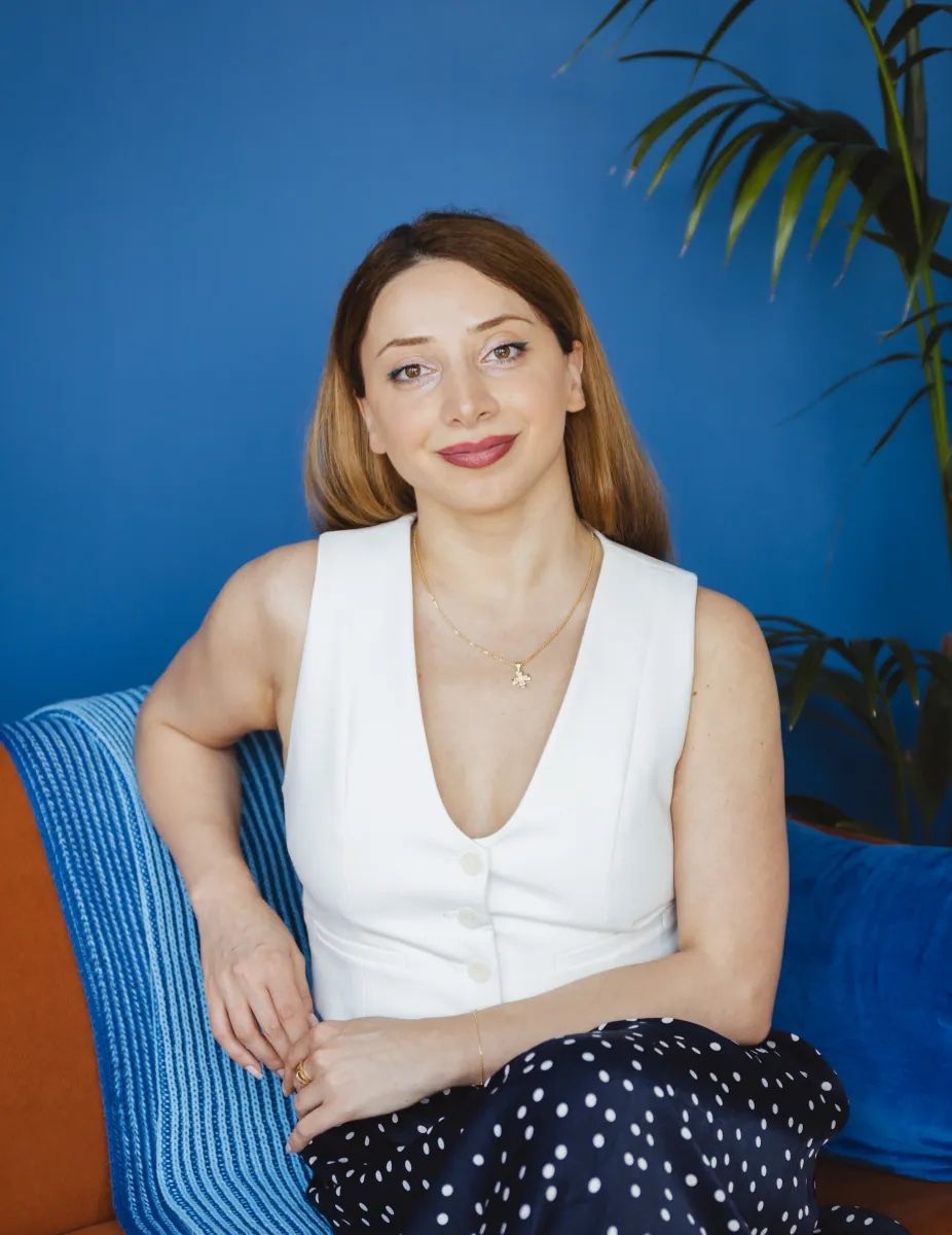 Nia, the founder of Nia Travel, seated in a white waistcoat against a deep blue wall